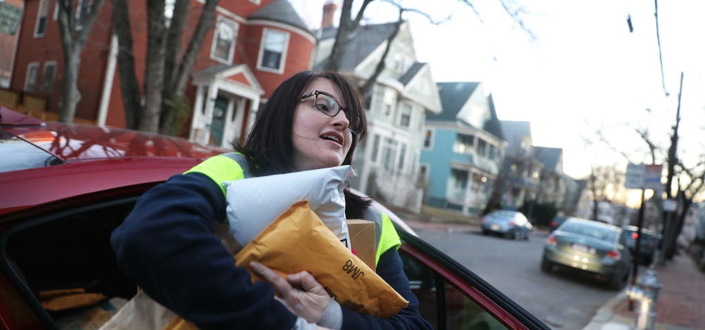 A photo of a gig worker delivering Amazon packages. She has a bunch of packages in her hands and is getting out of the car.