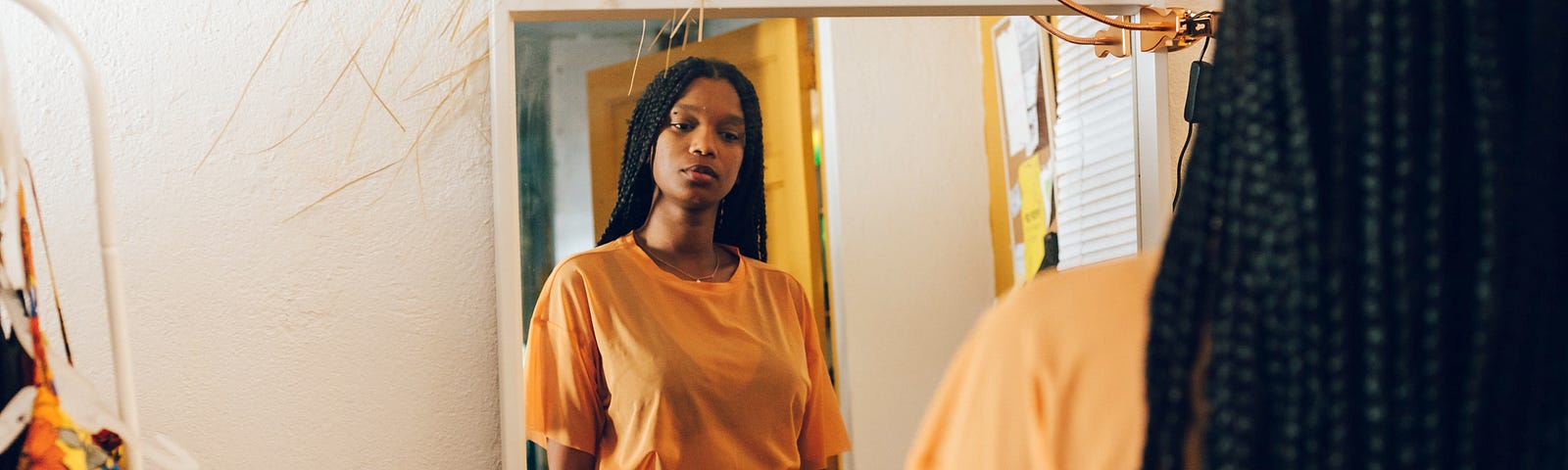 Young Black woman looking at her reflection in the mirror.