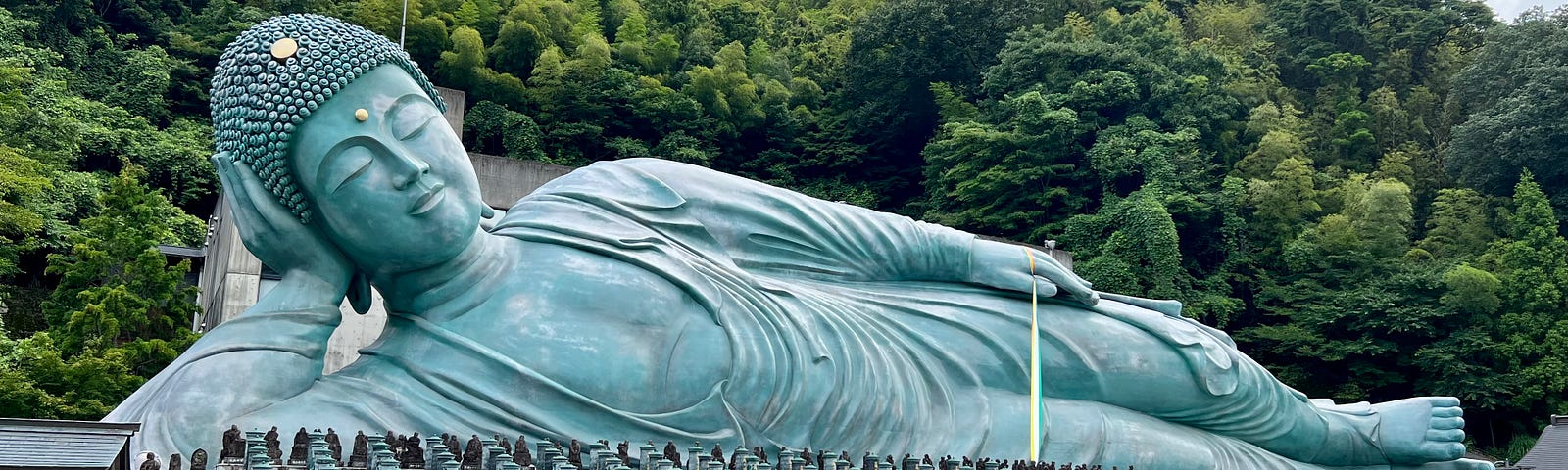 Reclining Buddha against a backdrop of green leafy trees.