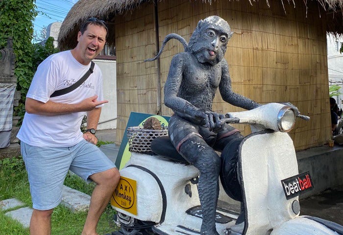 man standing next to statue of monkey riding a white scooter
