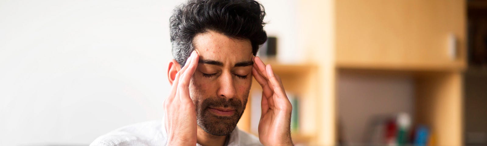 A man closes his eyes and massages his temples to relieve stress in front of his laptop.