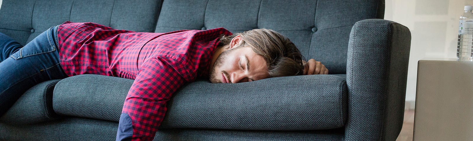 A photo of a sleeping man on the couch, laptop on the floor.