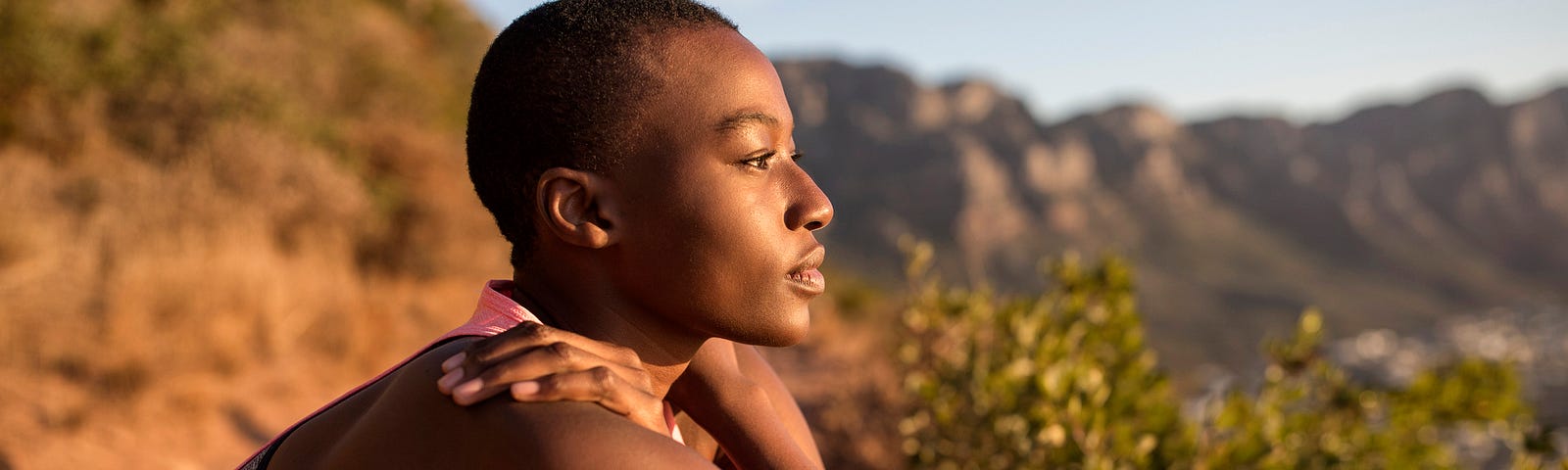 A photo of a peaceful black woman looking out at the view while taking a break on a hike.