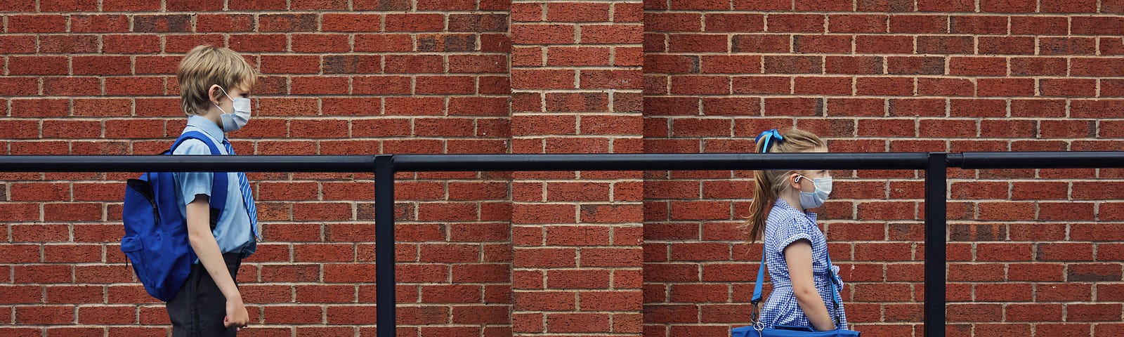 Two children wearing face masks standing six feet apart waiting in line for school.