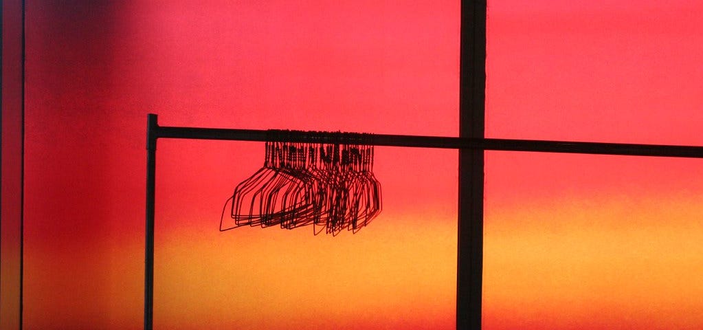 A bunch of clothes hangers hanging on a rack against a neon red/orange background.