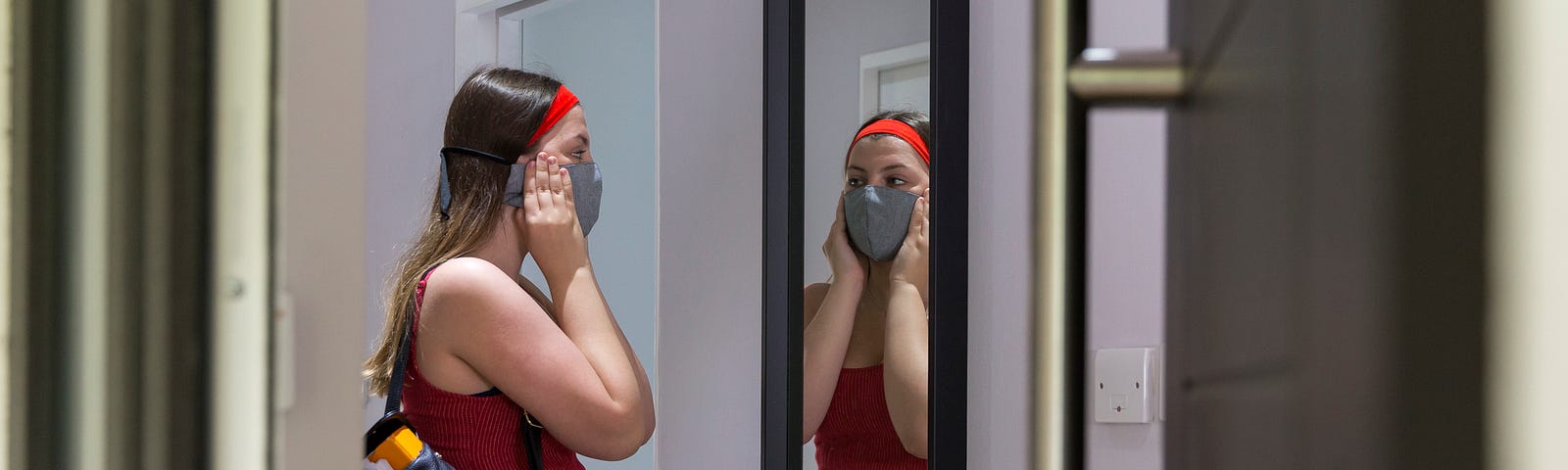 A photo of a girl putting on a face mask while preparing to go outside.