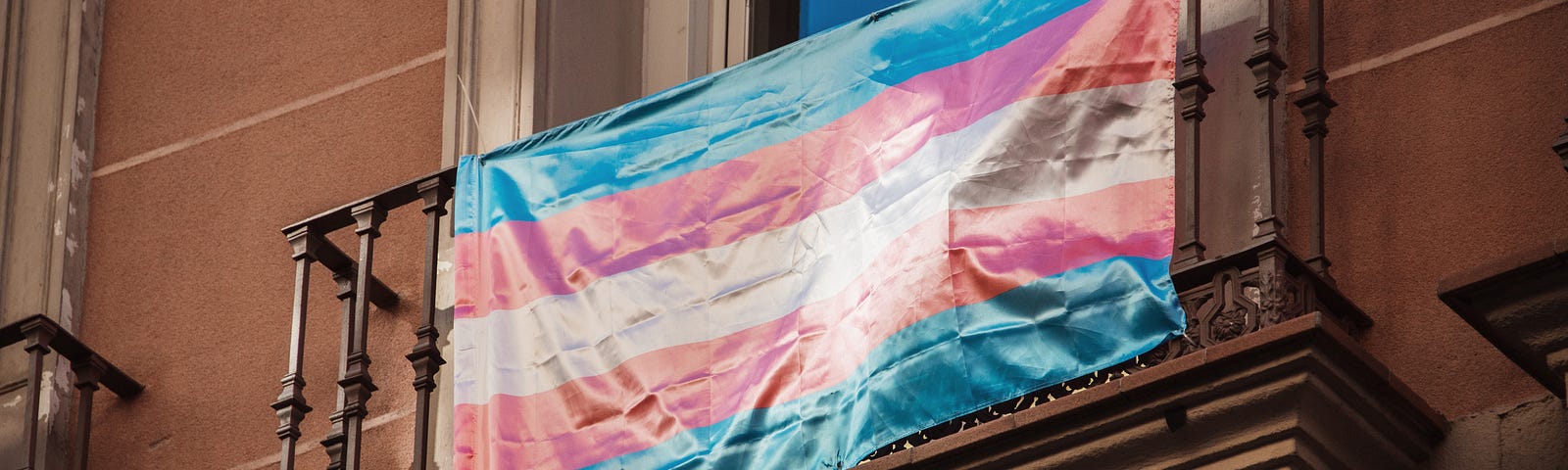 A photo of the trans flag hanging on a balcony.