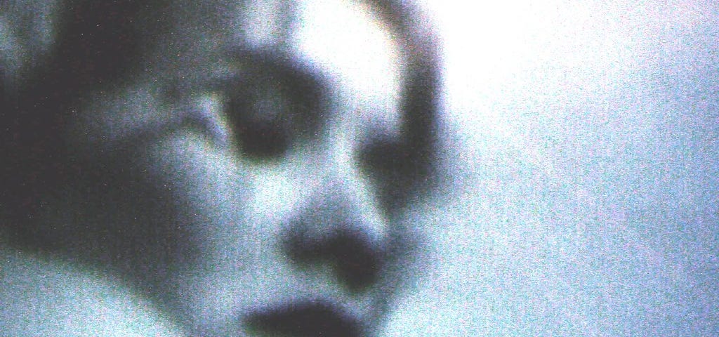 A grainy low-res photo of a woman with her eyes closed, seemingly resting her head on a pillow.