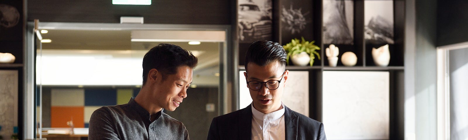 A photo of two men with their laptops talking about work in a cool office setting.