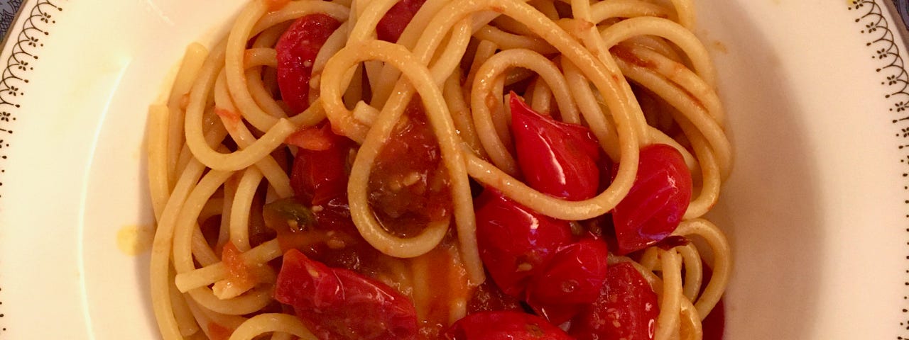 A bowl of pasta with fresh and cooked tomatoes.