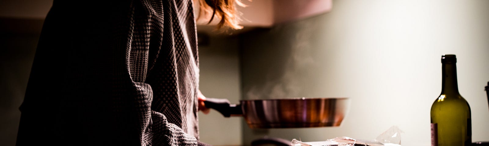 A dimly lit photo of a woman cooking on the stove top in her kitchen.