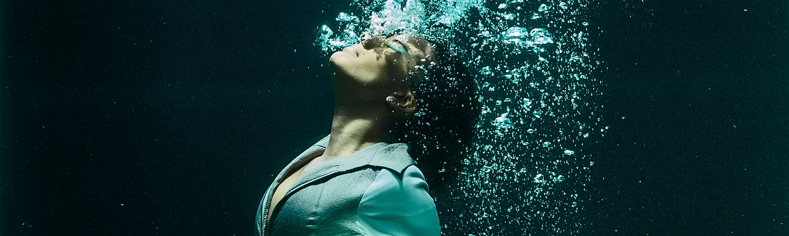 Woman under water, bubbles coming from her mouth. Dark, vertical photo.