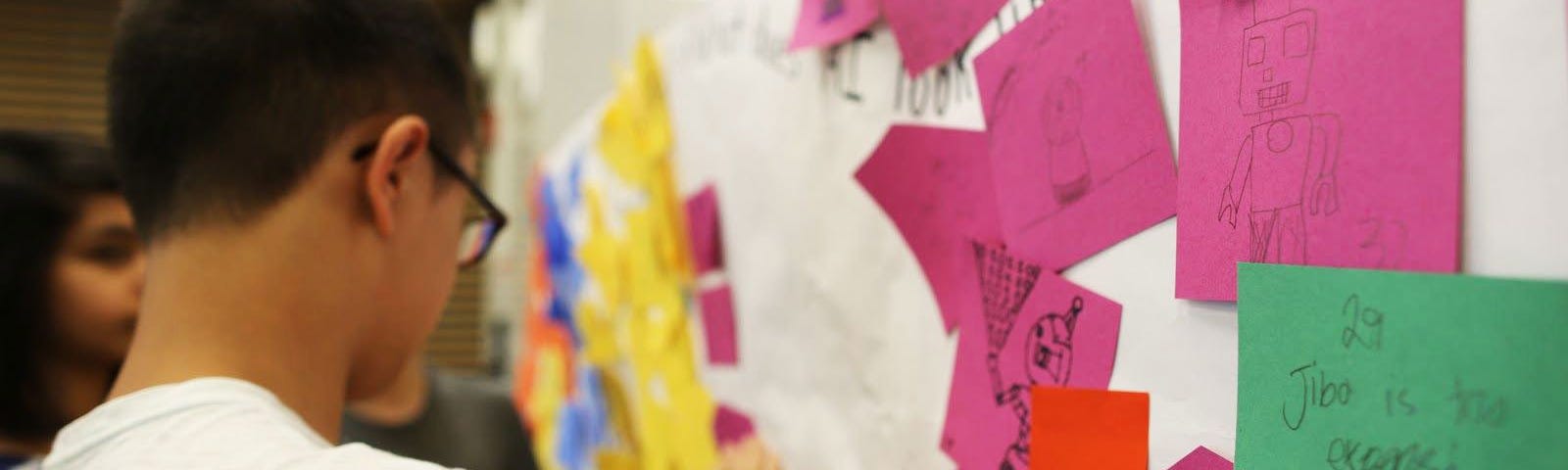 A middle schooler arranges magenta, orange, and green sticky notes on a whiteboard.