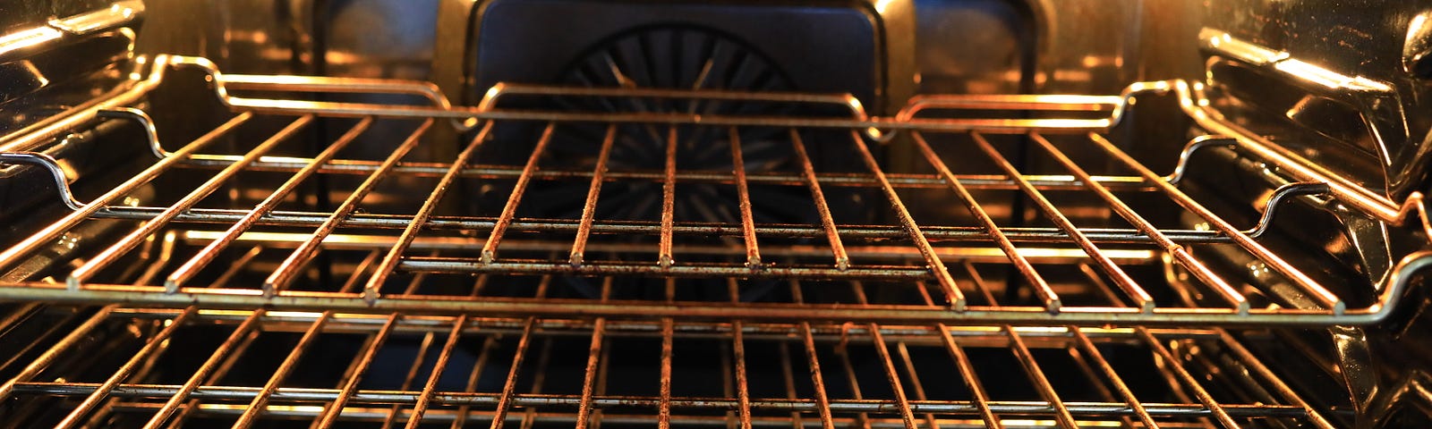 Empty racks inside an oven with its lights turned on.