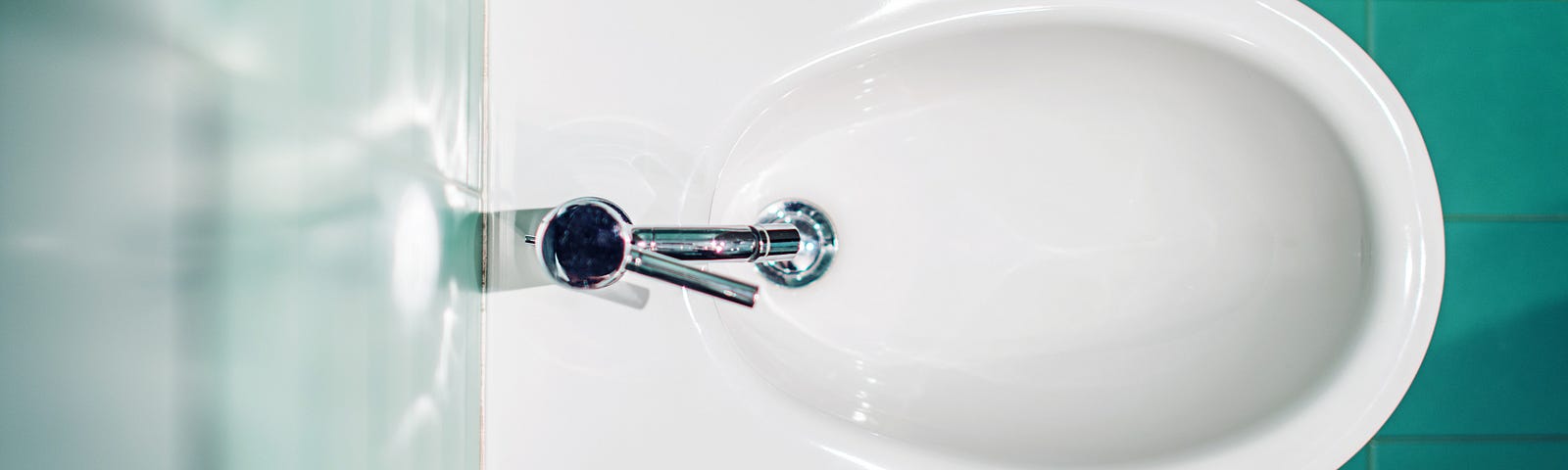 A top down view of a modern bidet fixture between emerald bathroom tiles.