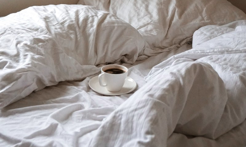 Cup of coffee on a small plate on a semi-messy bed.