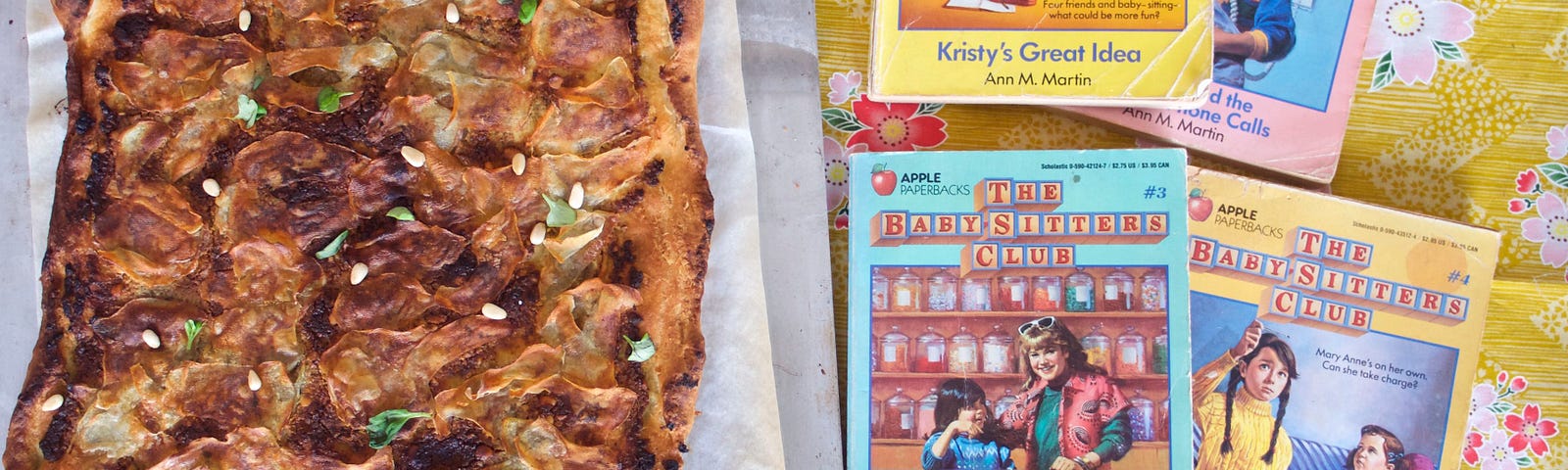 A rectangular sheet pan pizza with crispy, browned potatoes and basil and pine nuts, next to 4 retro Baby-Sitters Club books