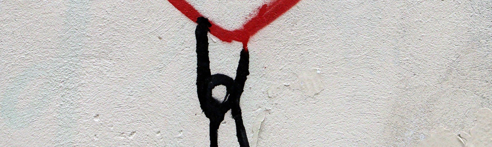 Graffitti of a red heart held upwards by a stick person on a cement wall