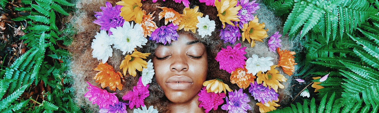 A photo of a Black woman with flowers in her hair against a leafy background.