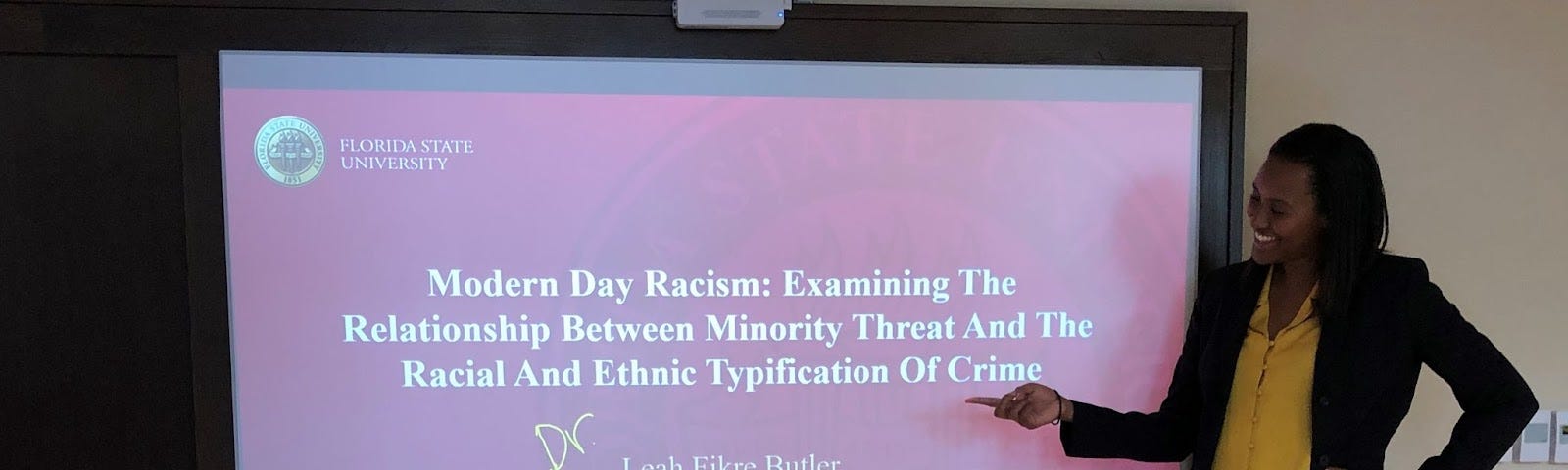 Leah Butler stands in front of a screen that shows her doctoral dissertation, “Modern Day Racism: Examining the Relationship Between Minority Threat and the Racial and Ethnic Typification of Crime.”