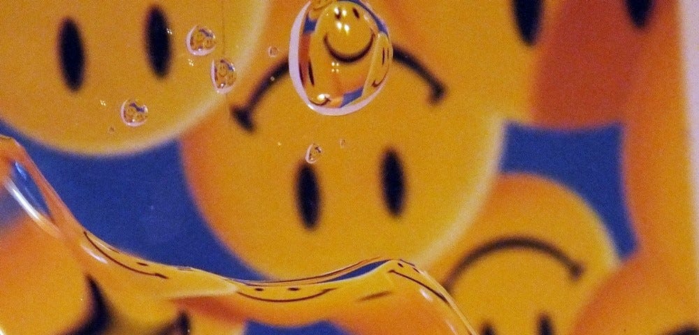 A photo of water droplets on glass with a reflection of upside down smiley face icons in the background.