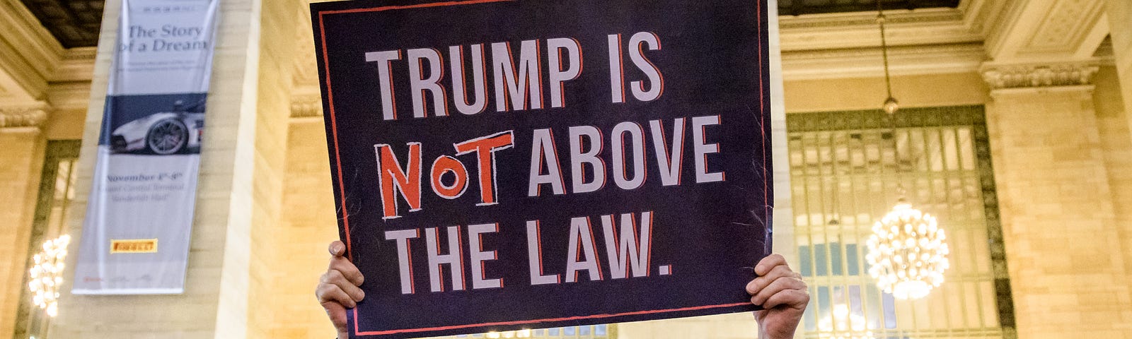 A protestor holds a sign that says “Trump is NOT above the law.”