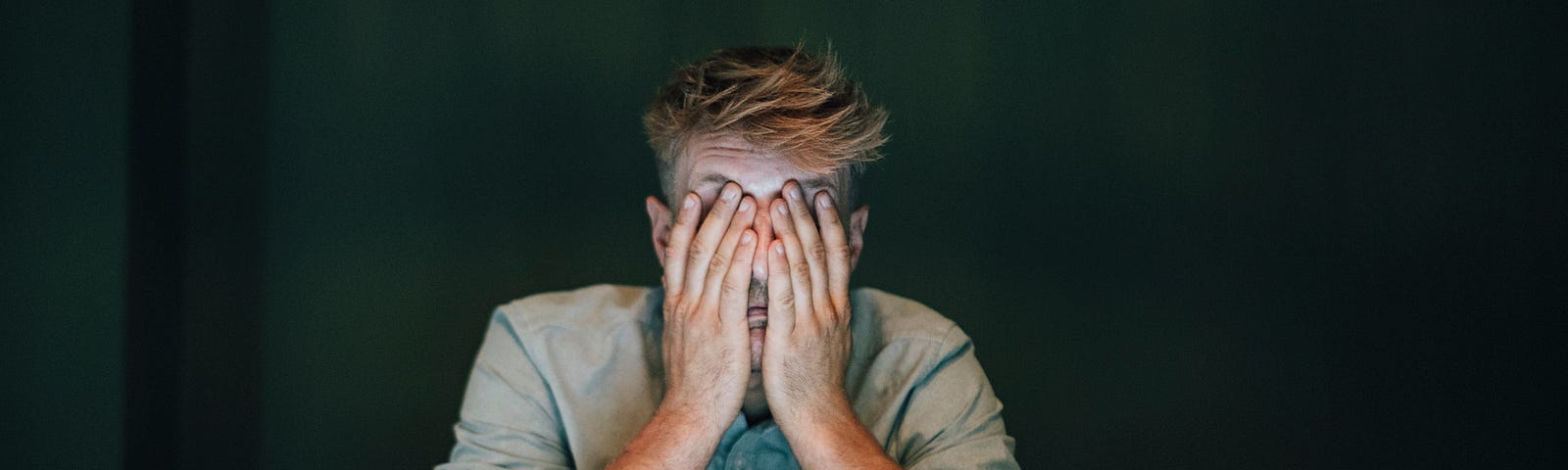 Tired exhausted man covering face with hands in front of laptop.