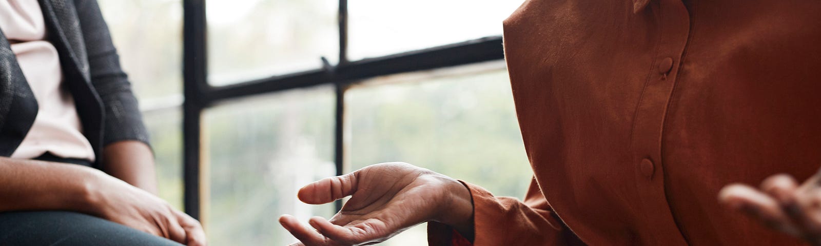 Midsection of businesswoman gesturing while sitting by window at workplace.