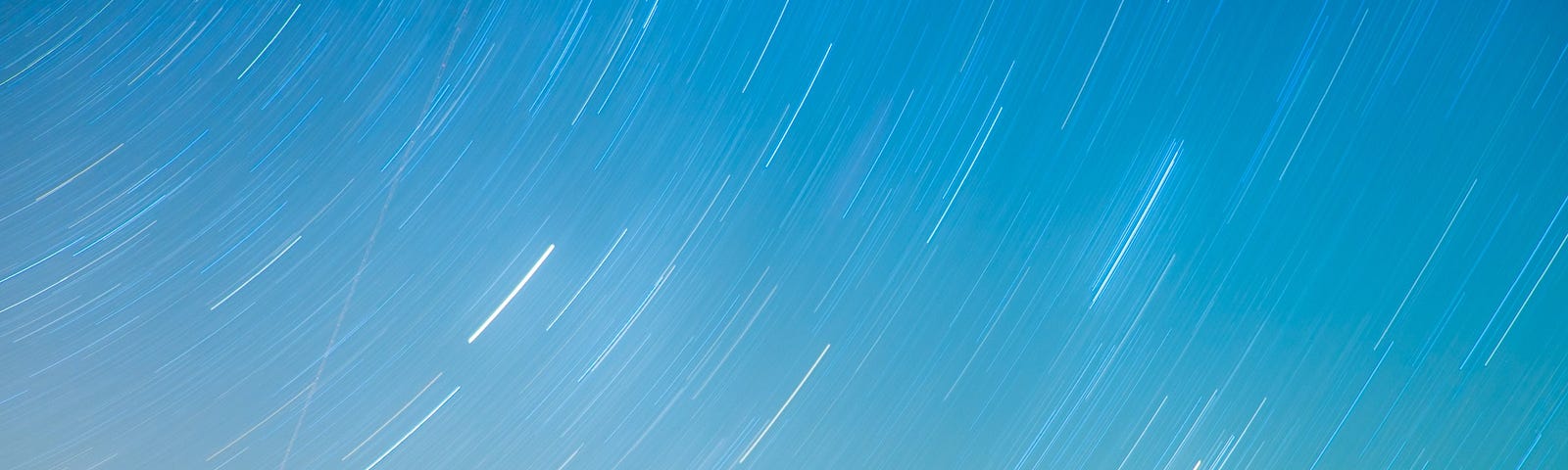 Timelapse photo of stars moving across the twilight sky in gentle upward arcs.