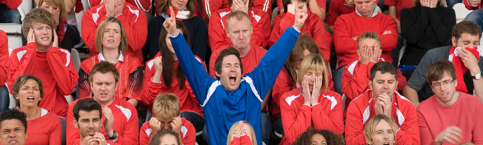 A fan wearing blue amongst rivals wearing red at a football match.