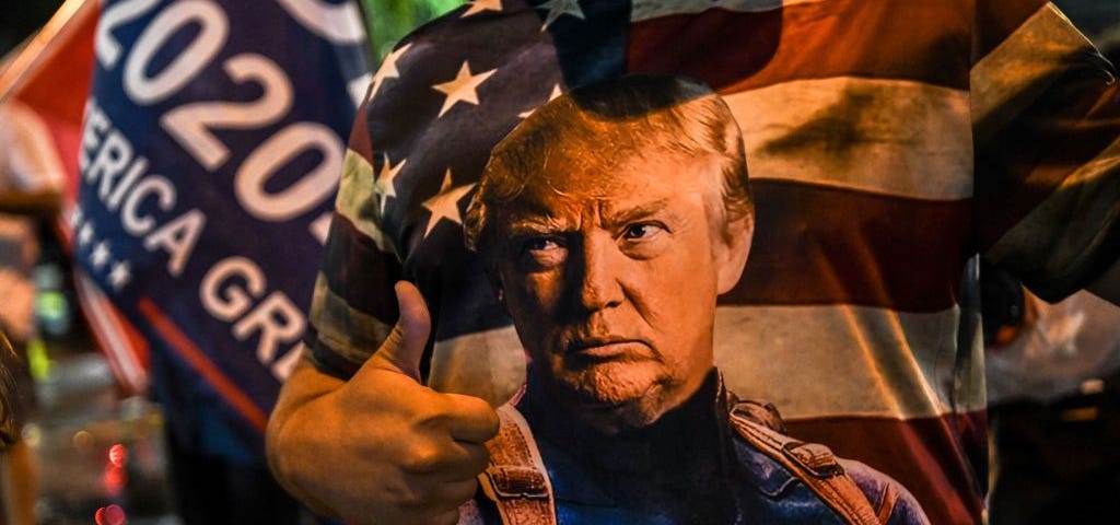 Trump supporter wears a shirt that has Trump as Captain America in front of American flag.