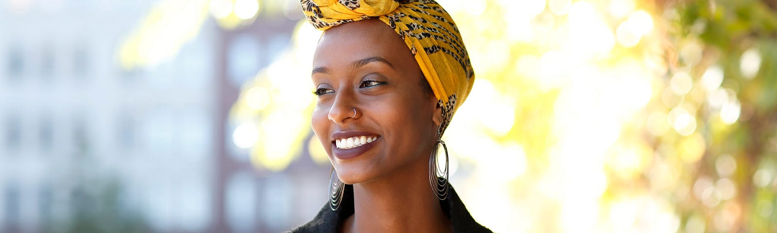 A portrait of a black woman outside in the sunlight, smiling