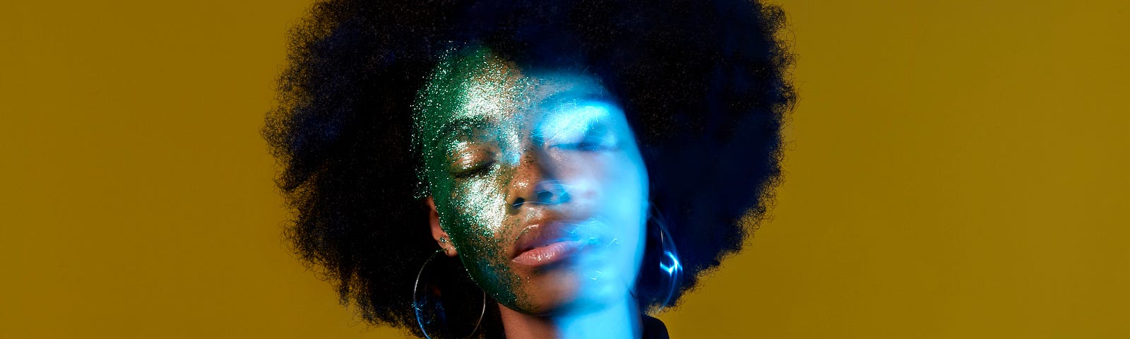 A conceptual portrait of a black woman with glitter on her face, with her face slightly blurred/double exposed.