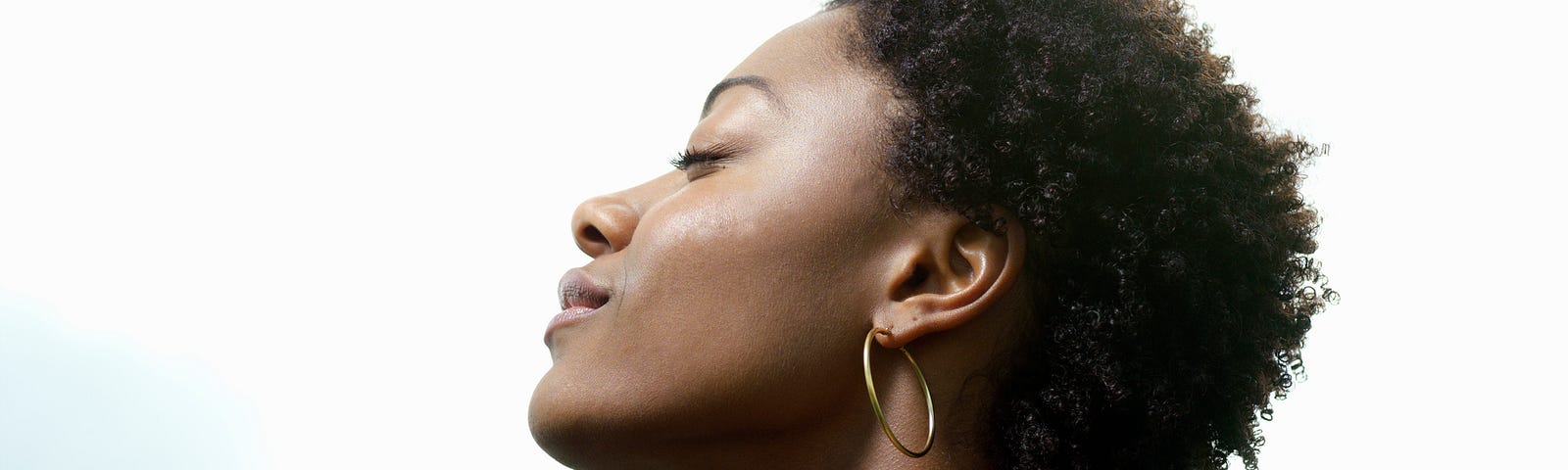 A photo of a black woman with her eyes closed, head tilted towards the sky, looking peaceful and serene.