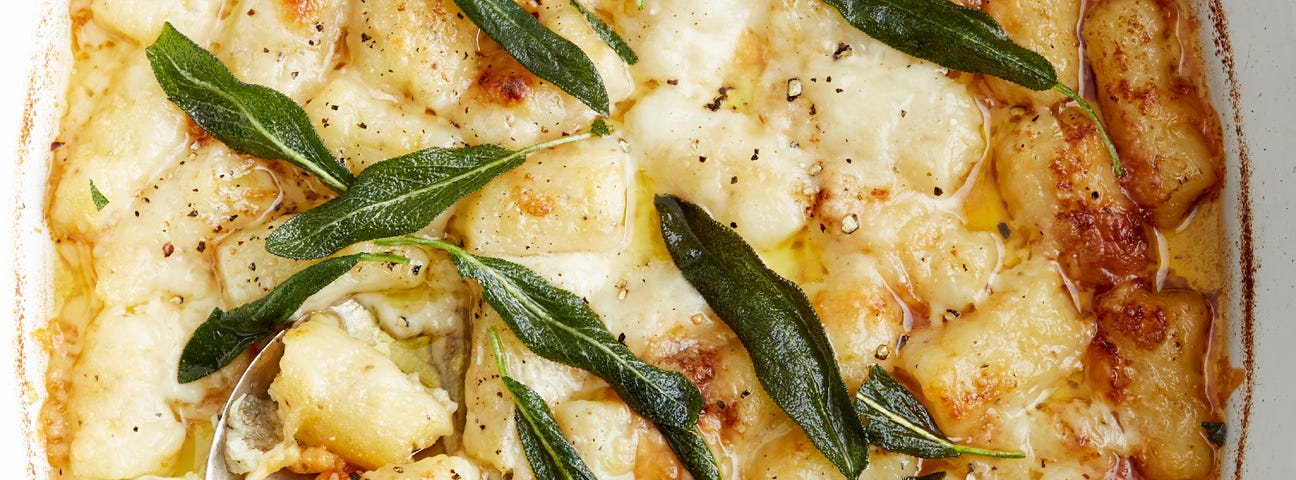 An oval casserole dish of gnocchi gratin garnished with crispy sage leaves.