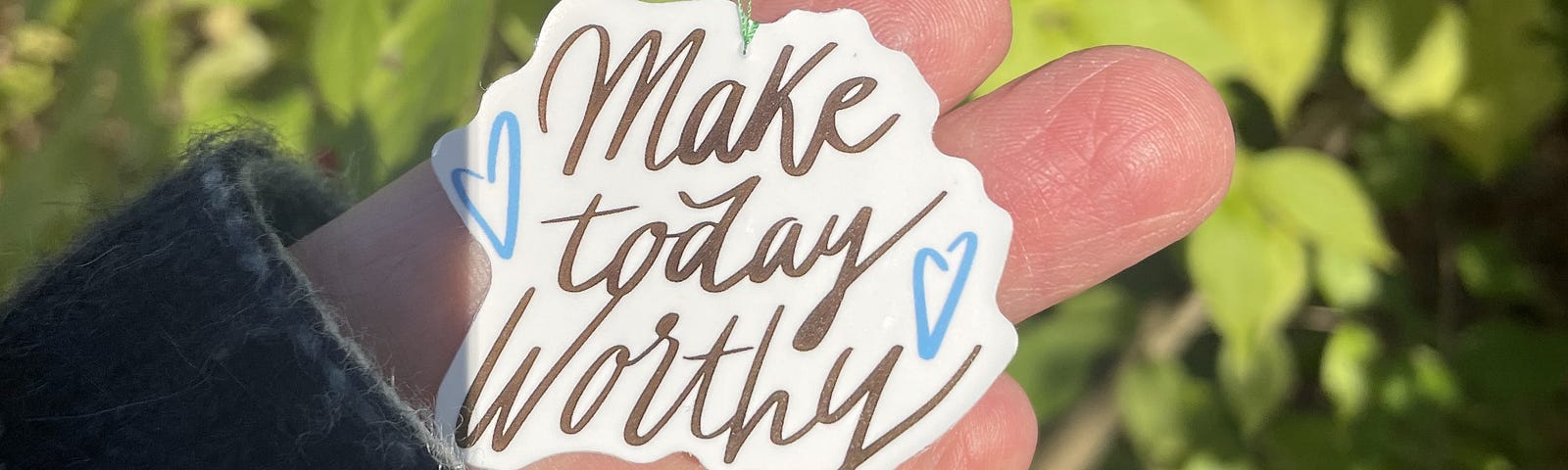 Tag hanging from a shrub branch that reads, “make today worthy.”