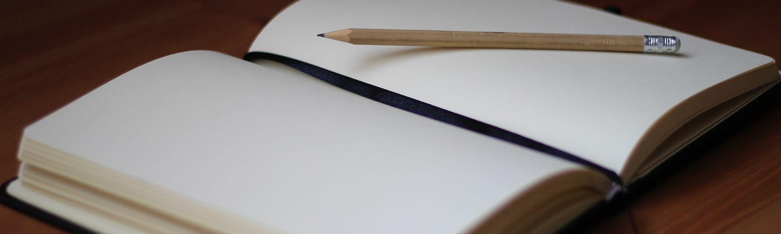 Photo of an open blank journal and penicl on a desk