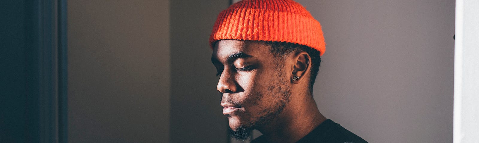 Young man wearing orange beanie closing eyes in peace.