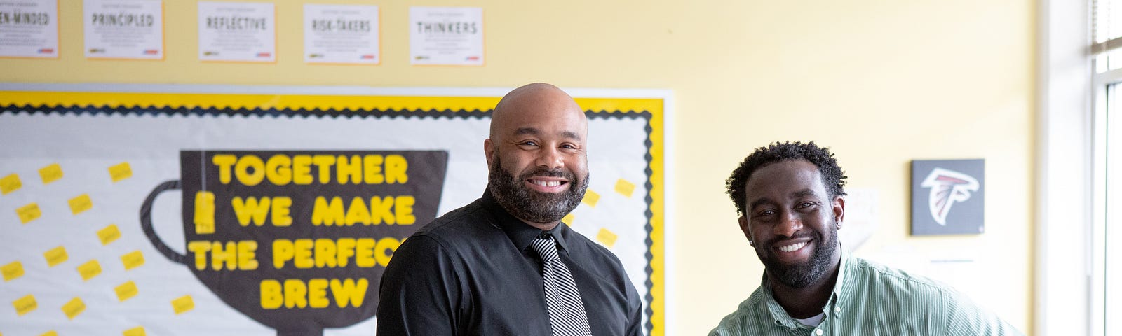 Two male teachers of color smile at the camera.