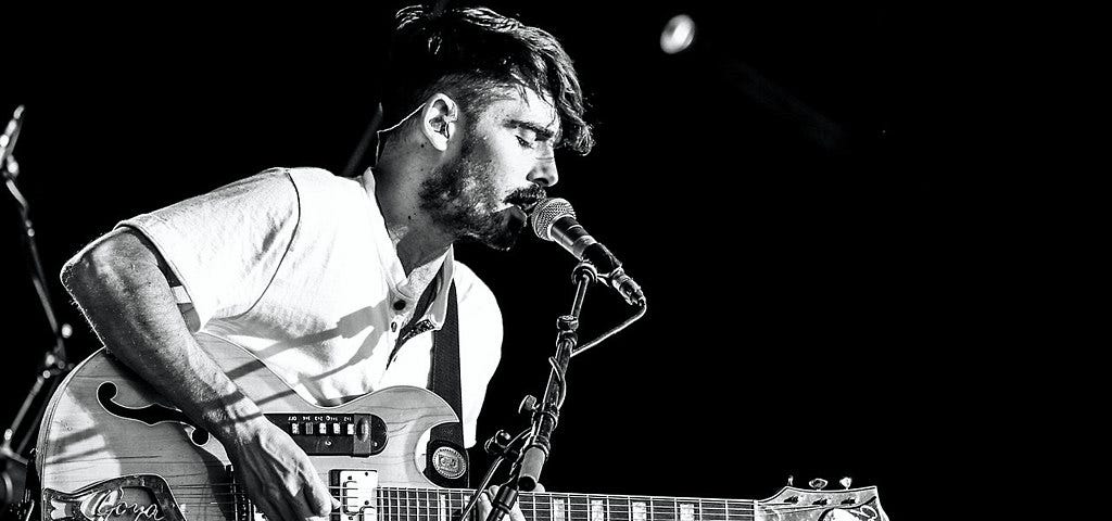 Man plays a guitar on stage and sings into a microphone