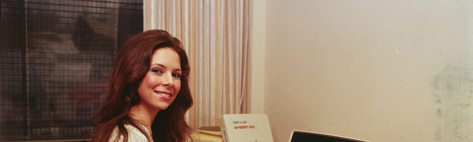 A woman works at an early model desktop computer made by Servus, circa the 1970s.