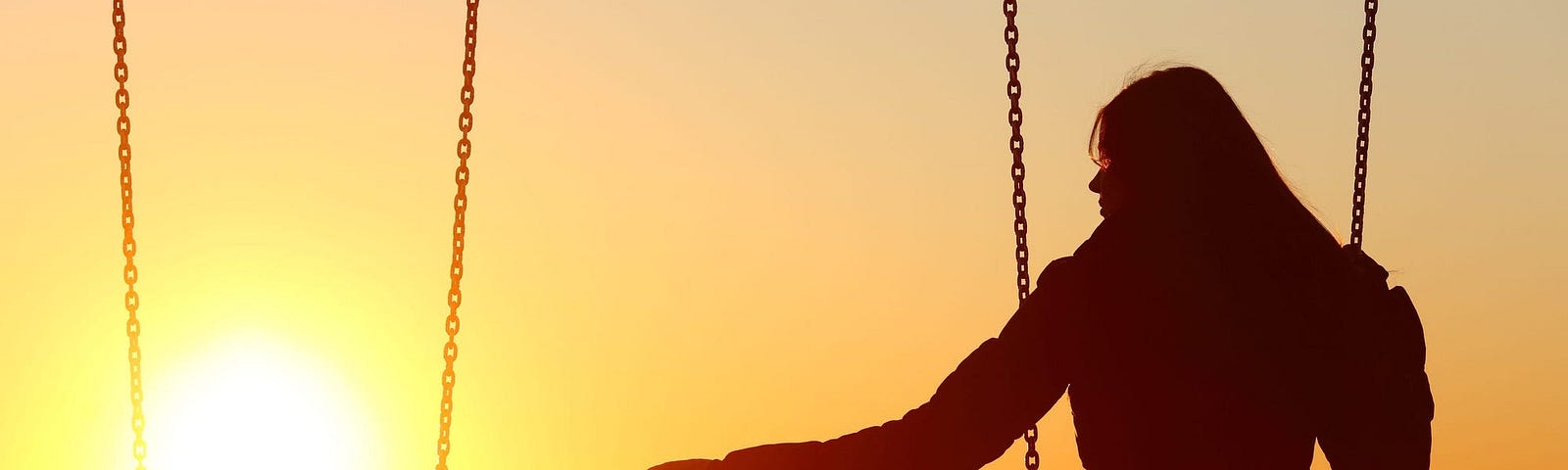 A person alone on a swing set watching the sunset.
