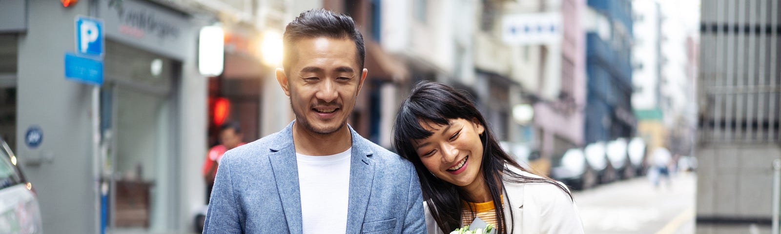 A photo of a happy Asian couple walking down the street. The woman is holding a bouquet of white flowers.