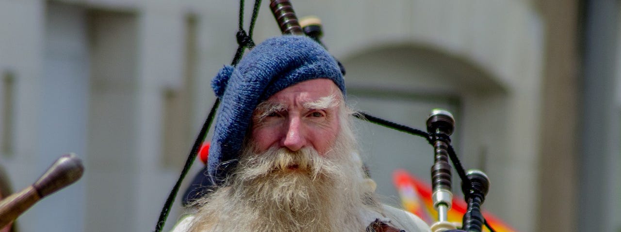 old Scottish man with a long white beard, a cap and bagpipes