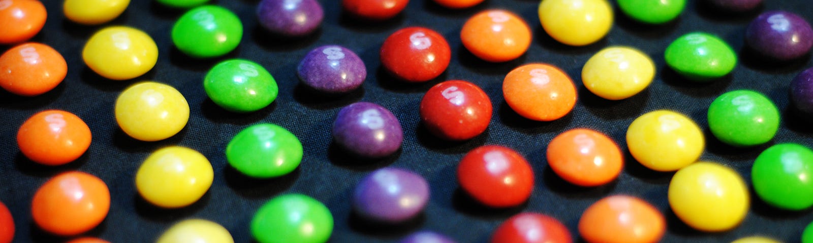 Neatly arranged lines of red, orange, yellow, green, and purple Skittles.