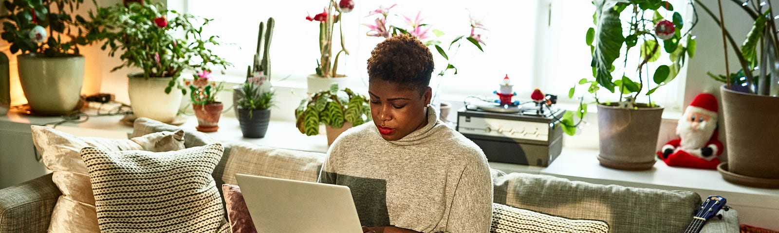 Black woman hard at work on her computer, sitting on her couch.