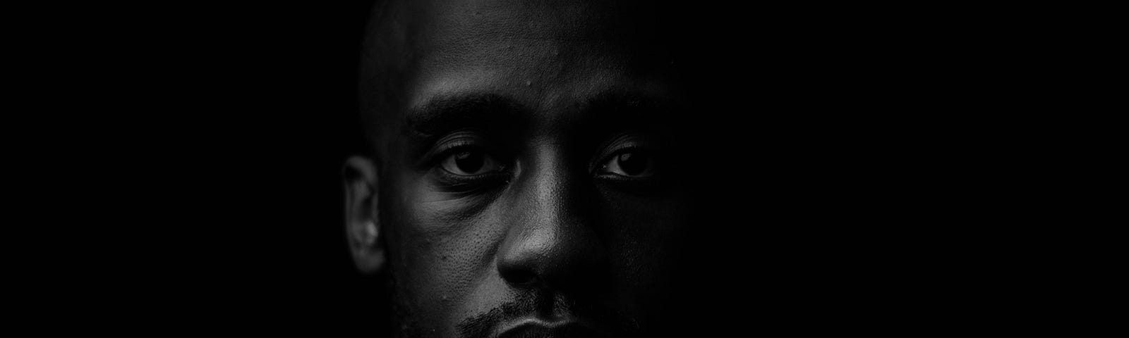 Close-up portrait of a young Black man against a black background.