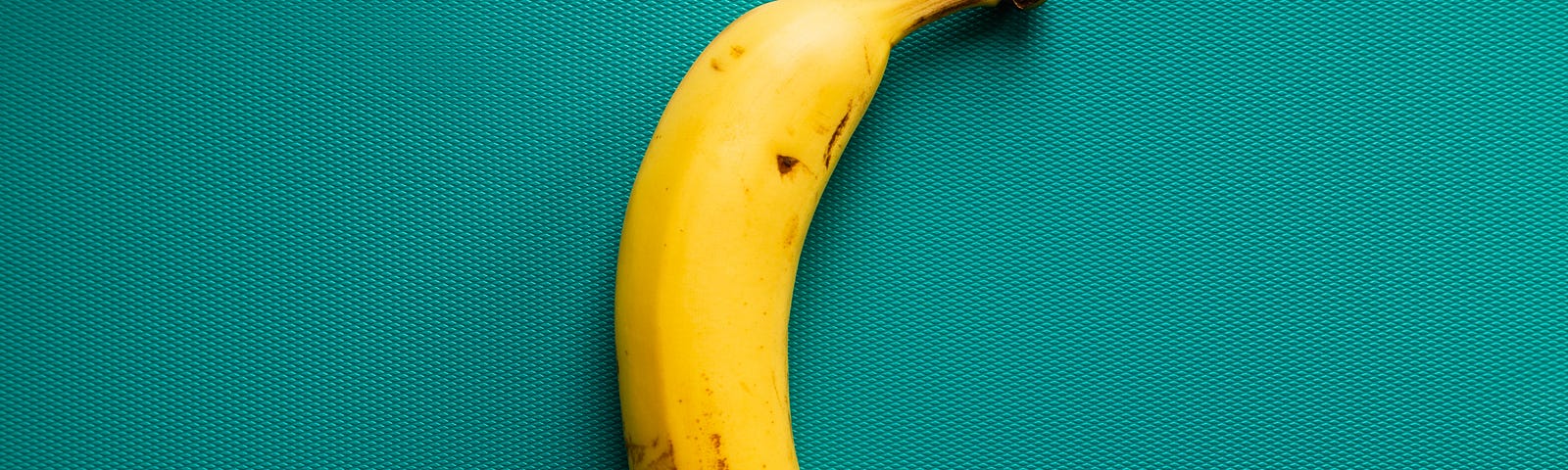 A photo of a banana against a teal background.