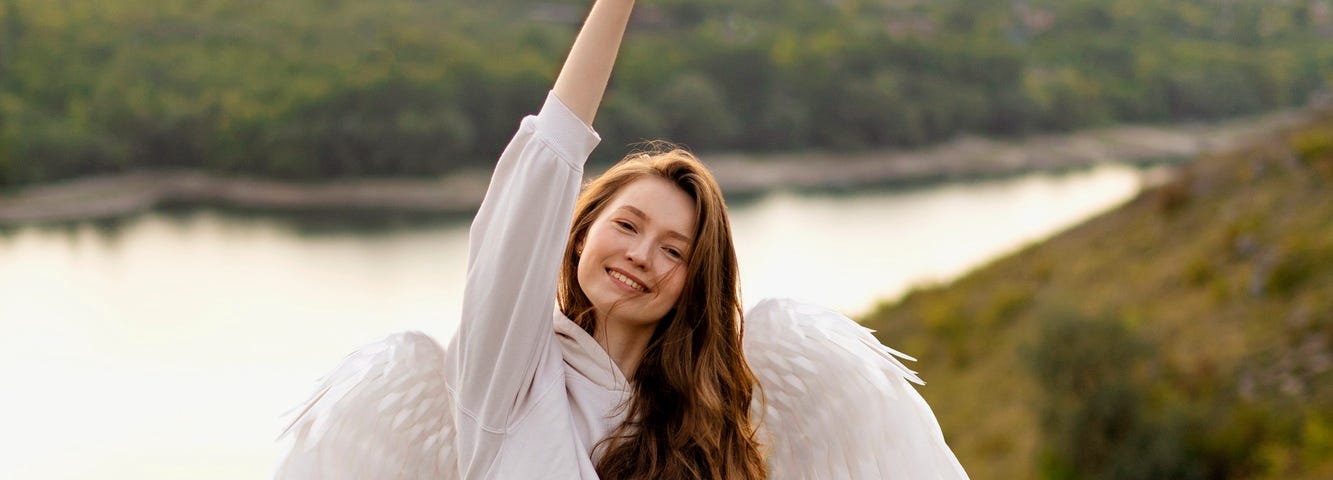 Angel with wavy brunnette hair and white clothing raising a glass of white wine. She is standing on a hill overlooking a river. The background is blurred, but the lighting gives a sense of serence peace to the overall picture.