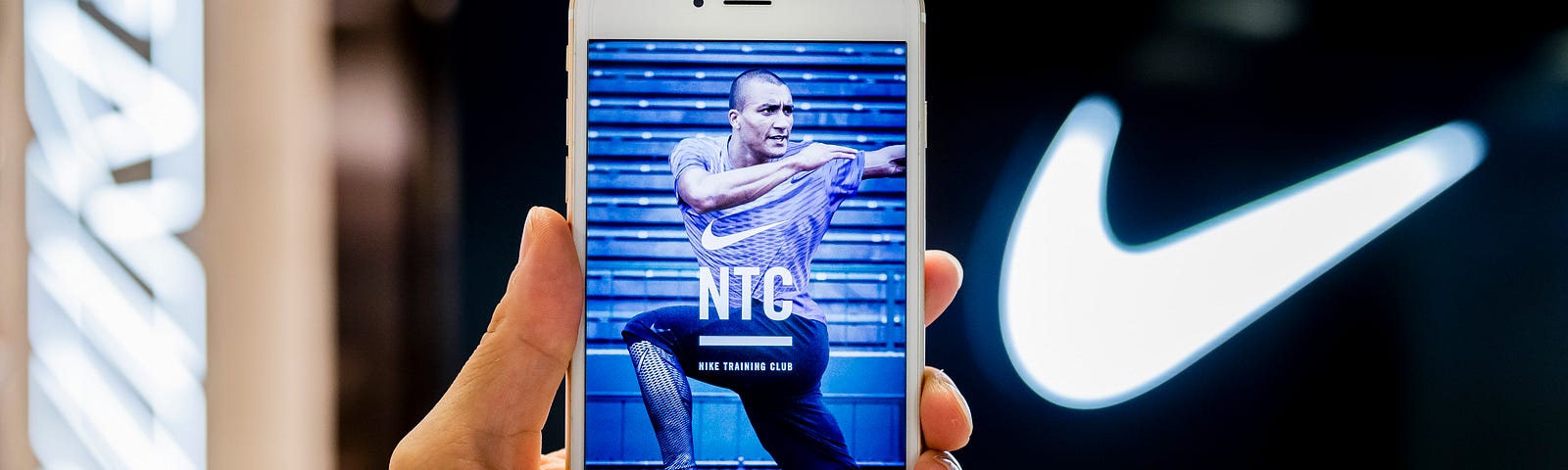 The Nike Training Club (NTC) app screen is displayed on a phone, held up against the Nike swoosh logo.